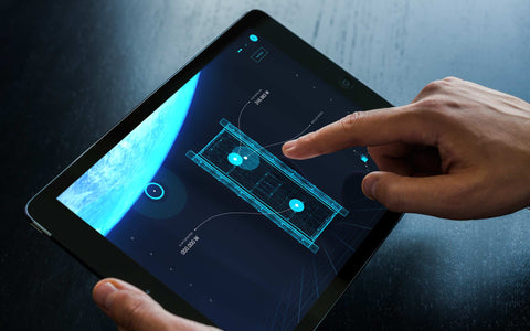 Professional using tablet displaying HIVE continuous mission operations interface with satellite diagram visualization and Earth view, showcasing SirCharles.DESIGN's 24/7 secure remote system capabilities for aerospace missions